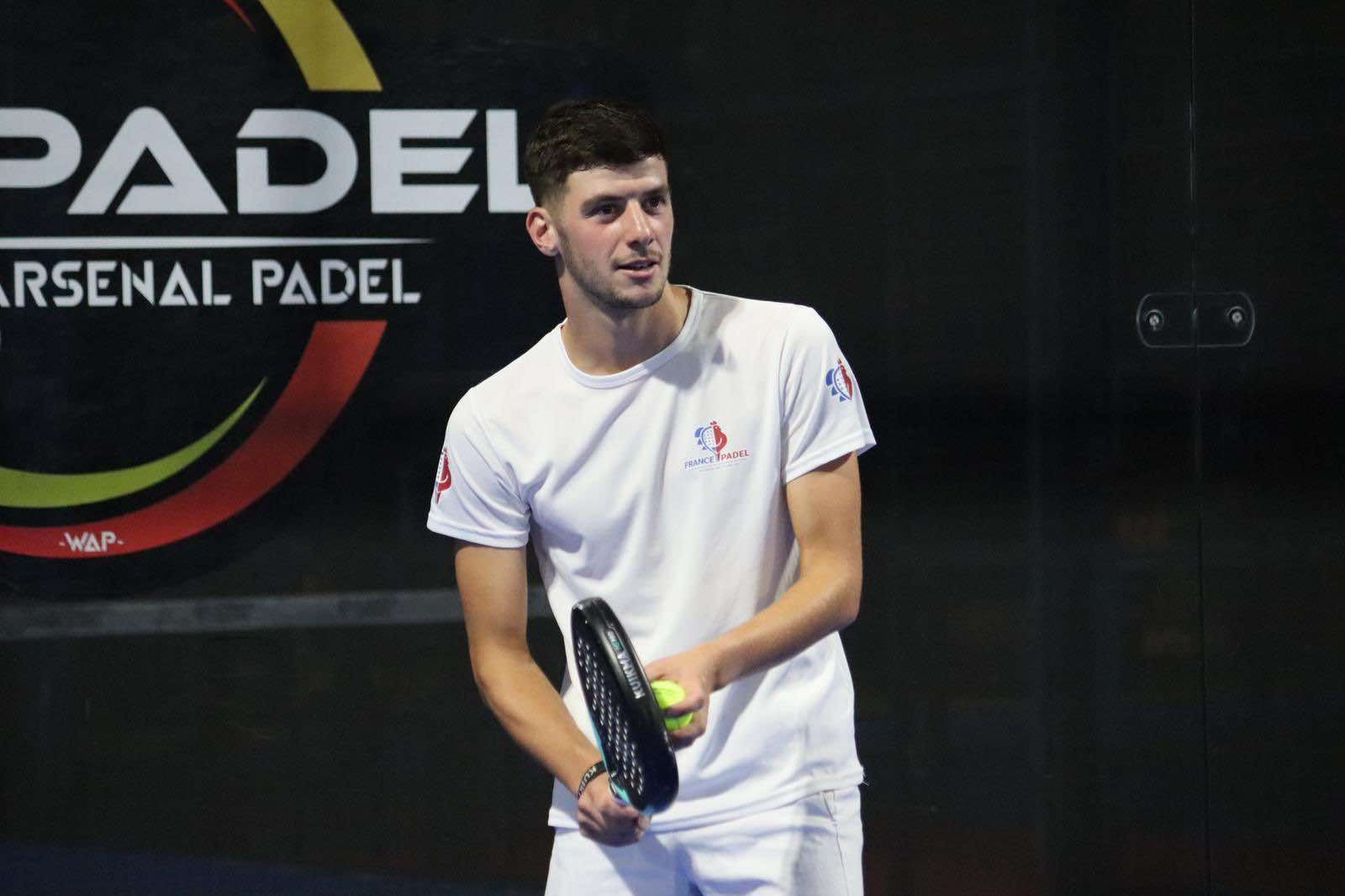 Padel player in white shirt holding racket and ball on indoor court.